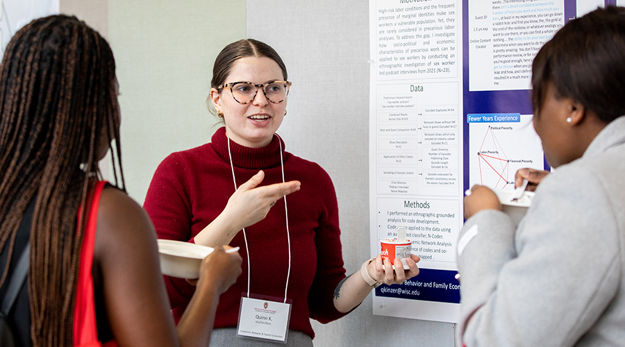 A graduate student presents their research to peers during a poster session.