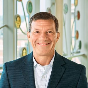Businessman with short dark hair, brown eyes, wearing a dress shirt and sport coat, and has a welcoming smile and friendly demeanor.