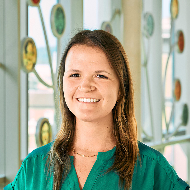 A white woman with brown, straight hair smiling, wearing a green shirt.