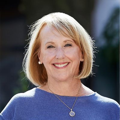 A white woman, with blonde bobbed hair, wearing a blue sweater.