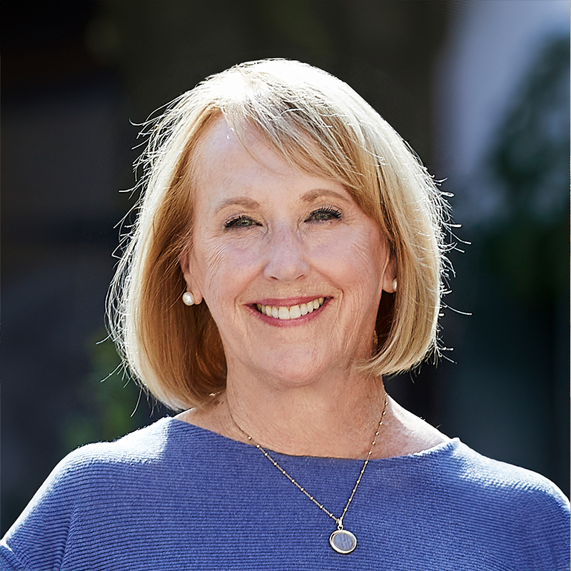 A white woman, with blonde bobbed hair, wearing a blue sweater.