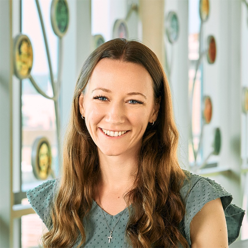 A white woman smiling, with curly, dark blonde hair and blue eyes, wearing a sage green shirt.