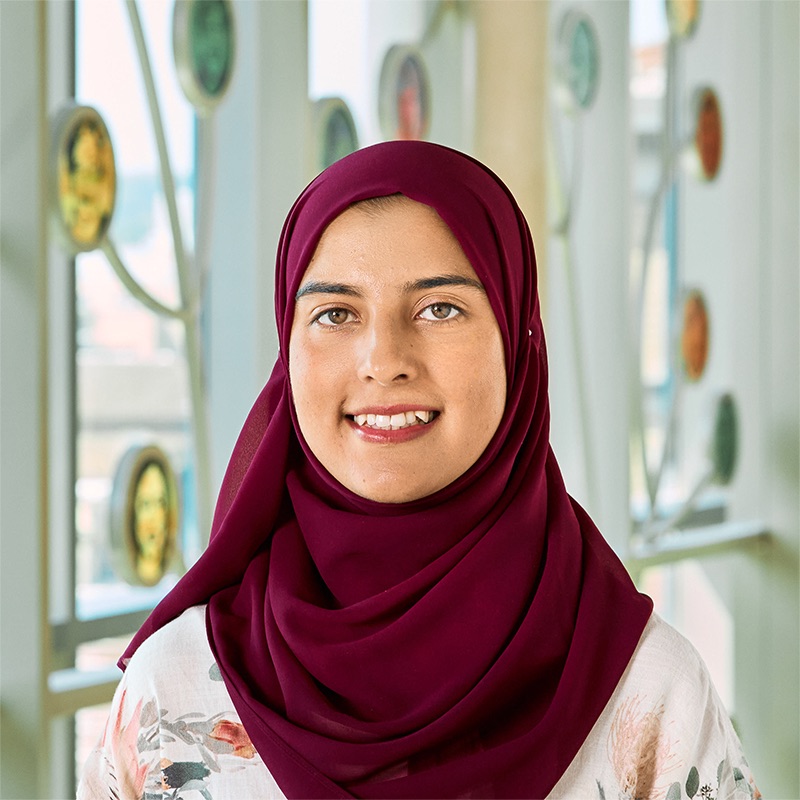 An Asian woman wearing a dark magenta headscarf with a white pastel shirt.