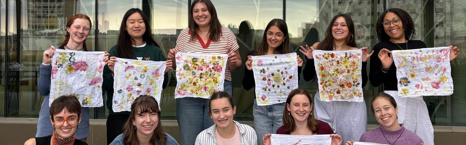 A group of students smile for the camera holding up textiles they created.