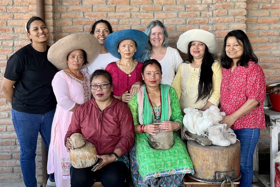 A group of nine people, several of whom are smiling, pose together for a photo. Three are wearing wide-brimmed felt hats.