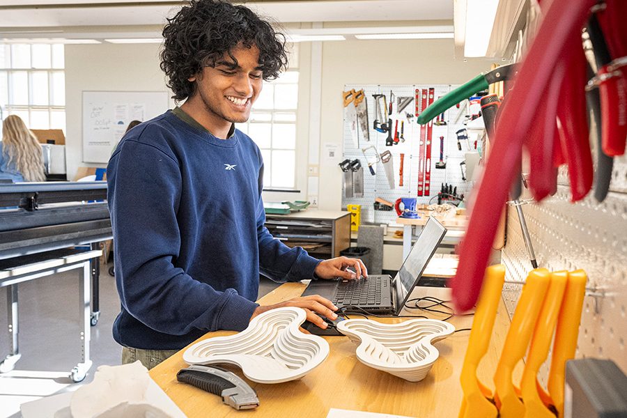 Anvay Das uses a laptop computer at a long workbench with 3D-printed materials and tools.