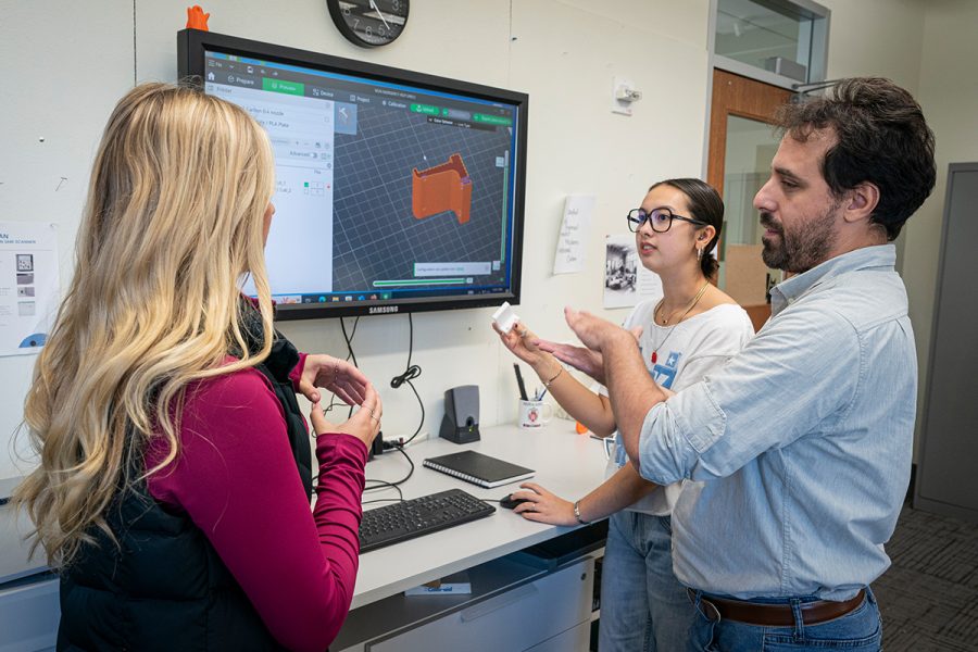 3 students standing around mounted computer screen having a conversation.