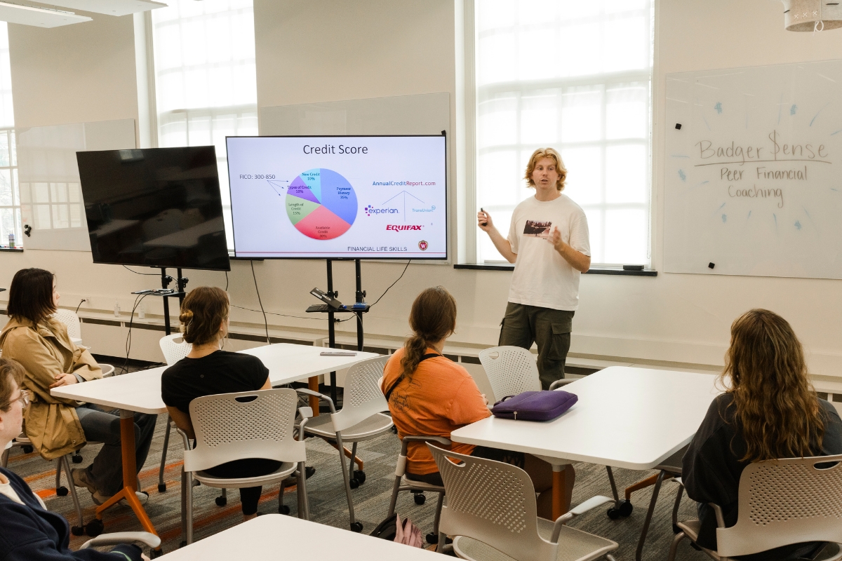 BadgerSense counselor stands and speaks to a classroom of workshop participants, pointing to a slide about Credit Scores.