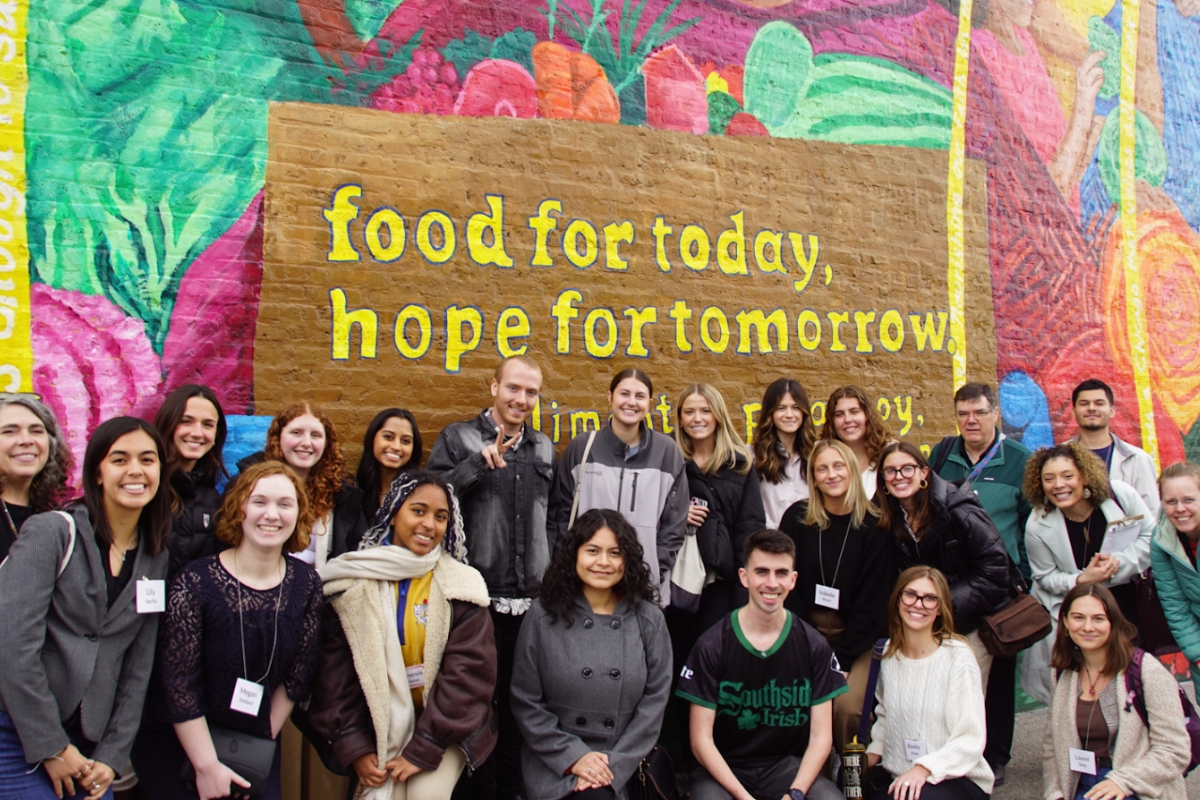 Group of people stands in front of a colorful mural that reads, "food for today, hope for tomorrow".