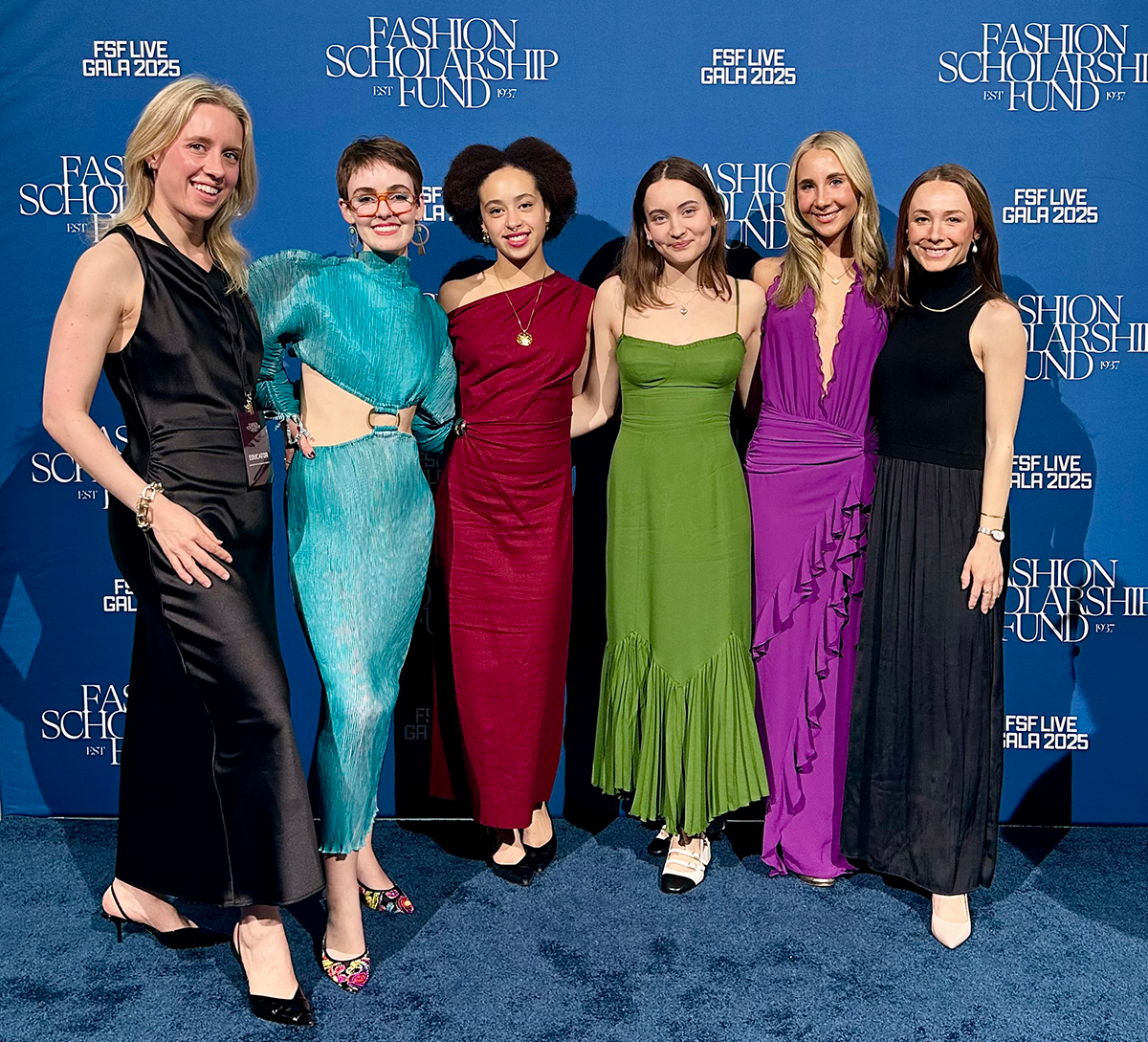 Six people in formal gowns stand and smile in front of a Fashion Scholarship Fund FSF Live Gala 2025 backdrop.