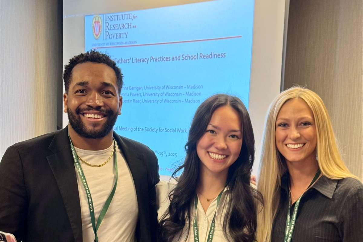 Three people wearing conference lanyards, stand in front of a slide presentation smiling.