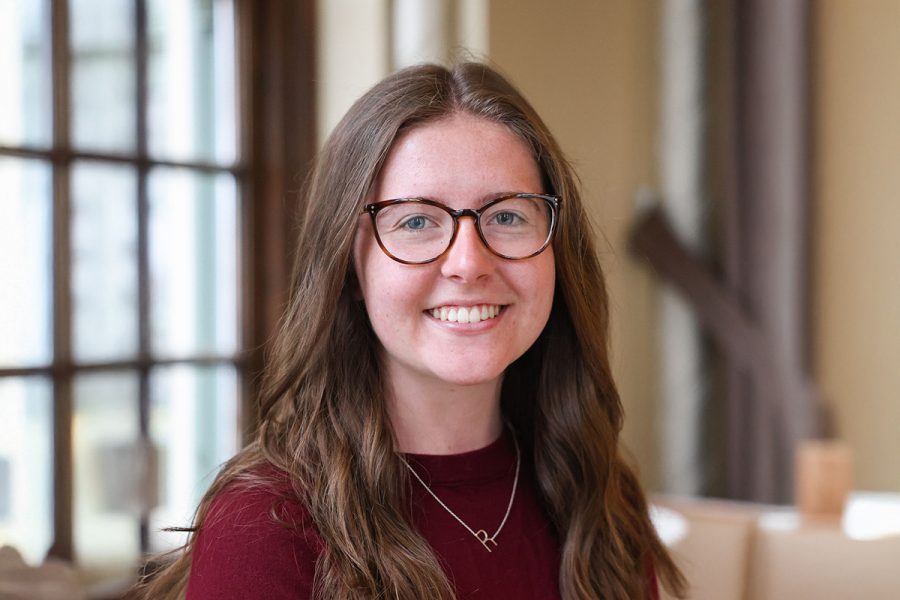 Person with brown, long hair, blue eyes and glasses smiling.