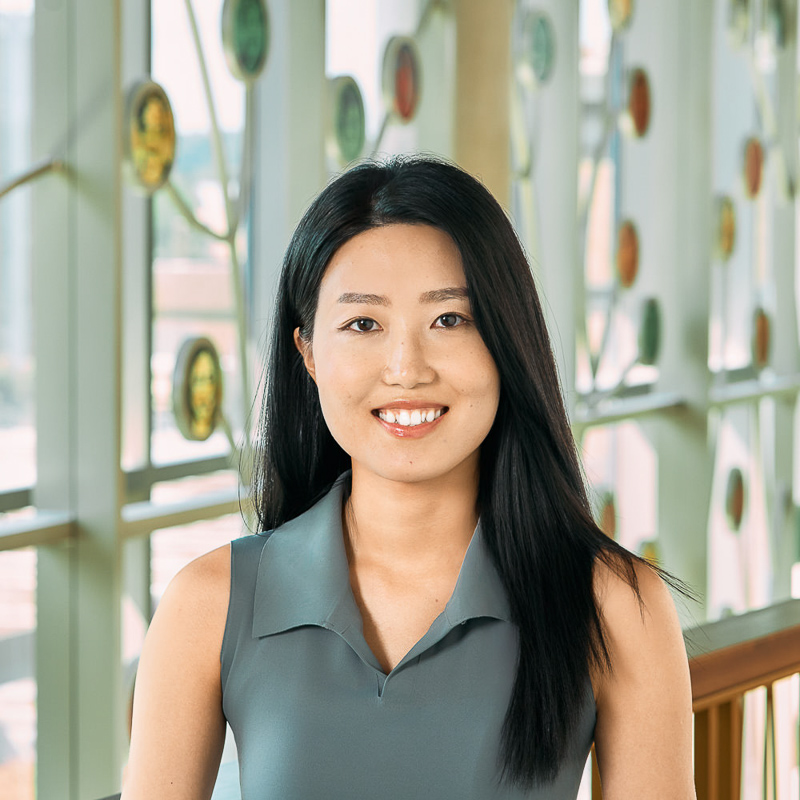 An Asian woman smiling, with long black hair, wearing a gray short sleeve.