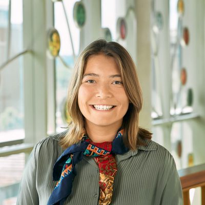 A white-Asian woman smiling, with brown hair, wearing a green blouse and a colorful scarf.