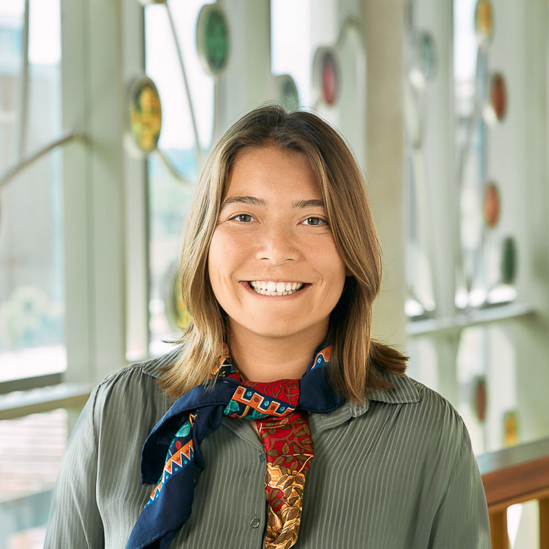 A white-Asian woman smiling, with brown hair, wearing a green blouse and a colorful scarf.
