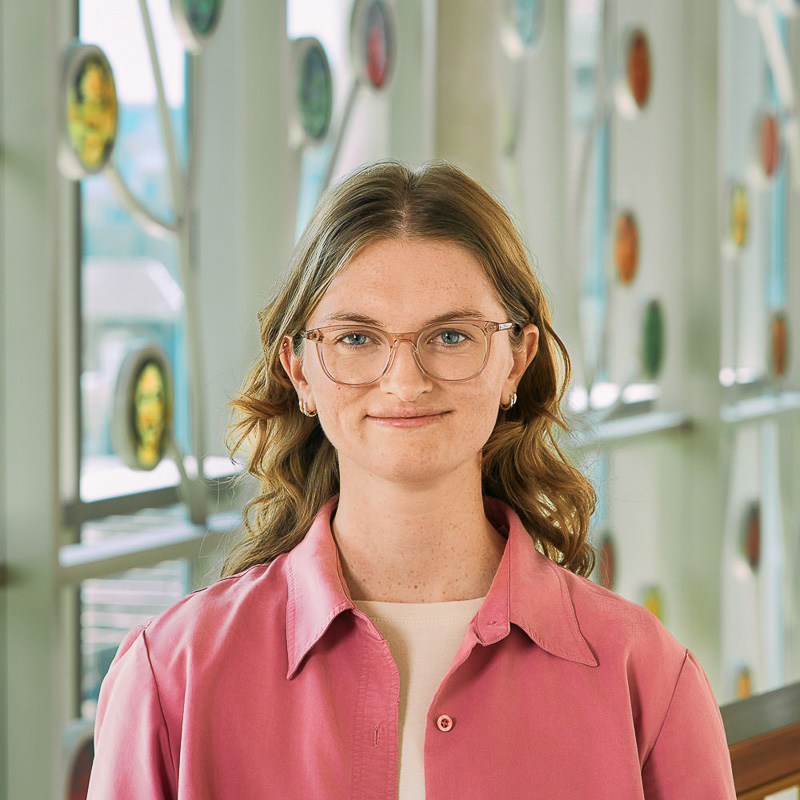 A white woman with brown hair wearing a pink shirt.
