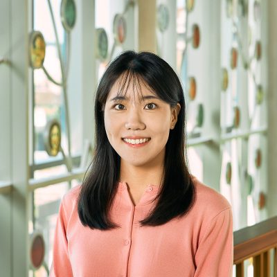 An asian woman smiling, with shoulder-length black hair, wearing a pink shirt.
