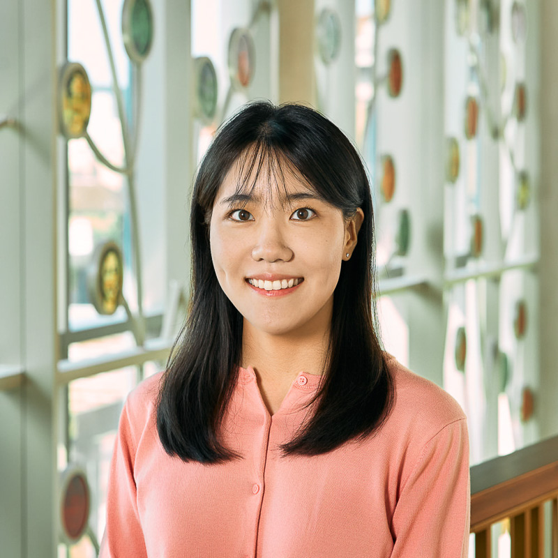 An asian woman smiling, with shoulder-length black hair, wearing a pink shirt.