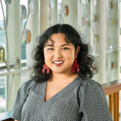 An South East Asian Woman with shoulder length, curly hair, smiling, wearing lobster earrings and a seashell top.