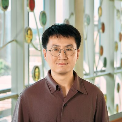 A Chinese man smiling, with a black hair and wine red T-shirt.