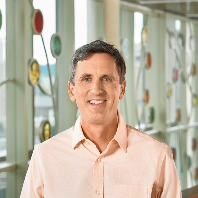 A white man smiling, with short brown hair, wearing a light orange shirt.
