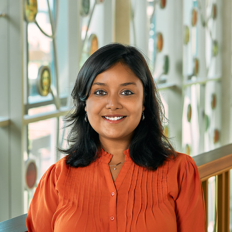 A brown woman, with a orange top, and blue earrings.