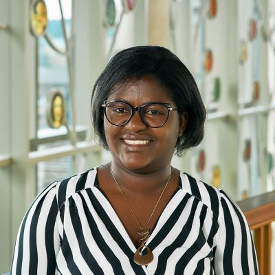 A Black lady wearing a black and white striped shirt and cat eye glasses.