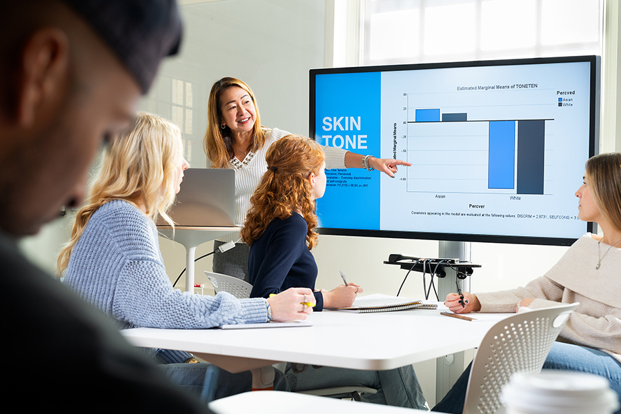 Faculty member teaching a class to students and pointing at graphic on a screen.