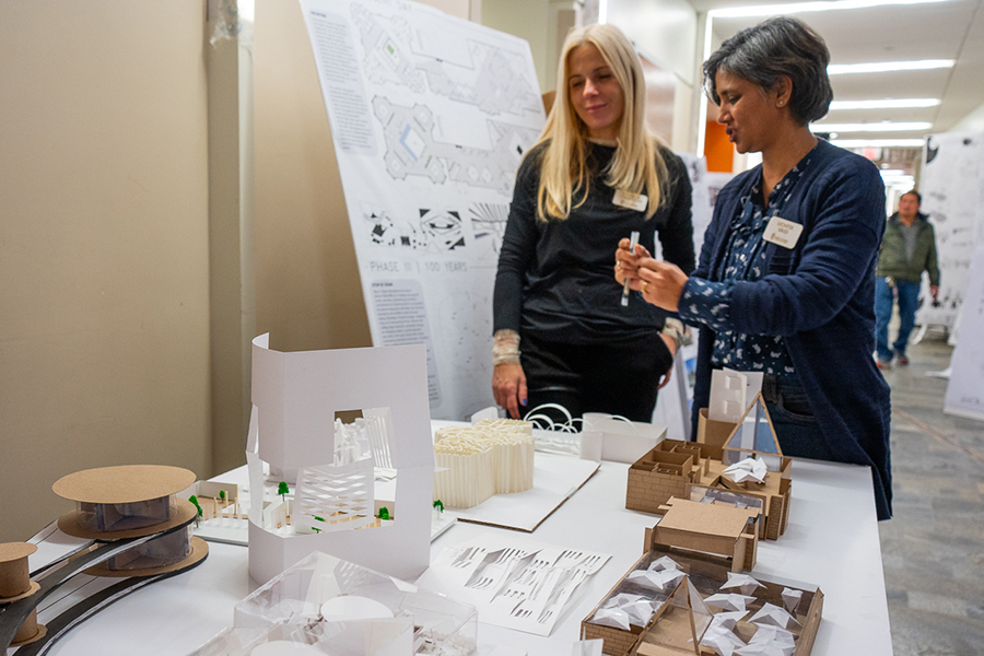 Two instructors discuss architectural models on a table in front of them.