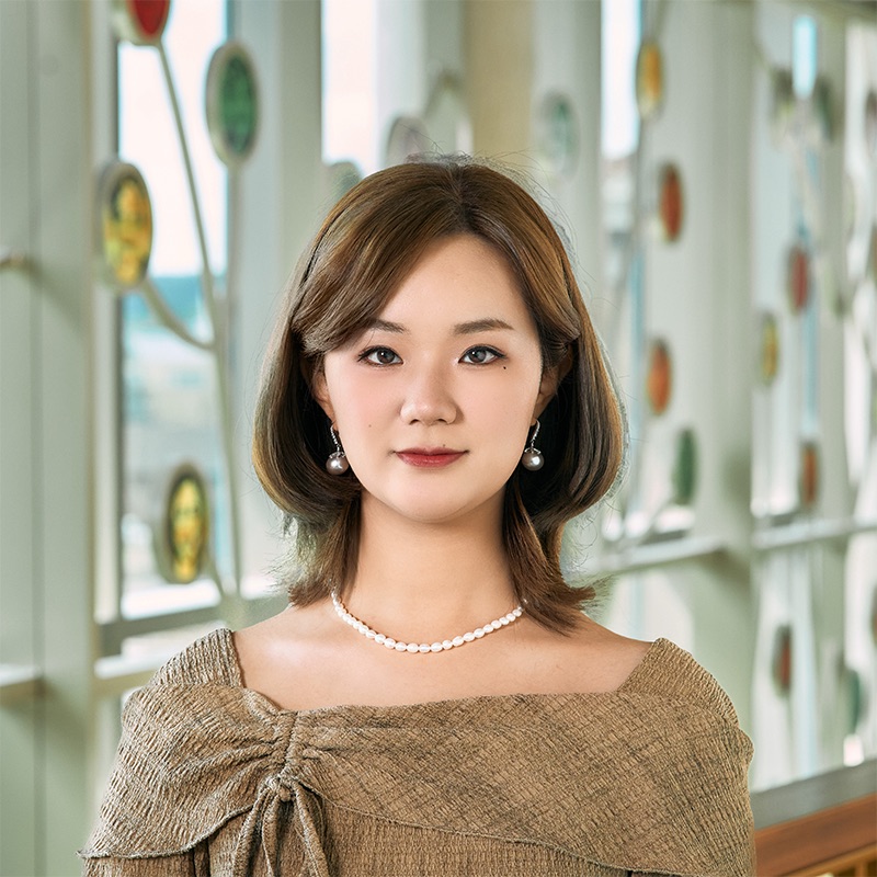 A Chinese woman smiling, with short brown hair, wearing a pearl necklace and earrings.
