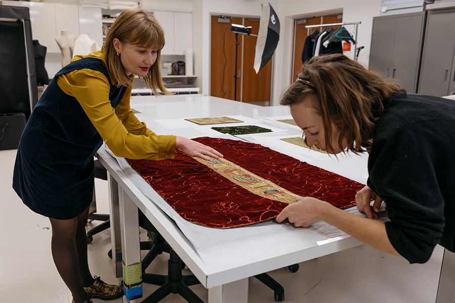 Two people studying a textile object on a white table.