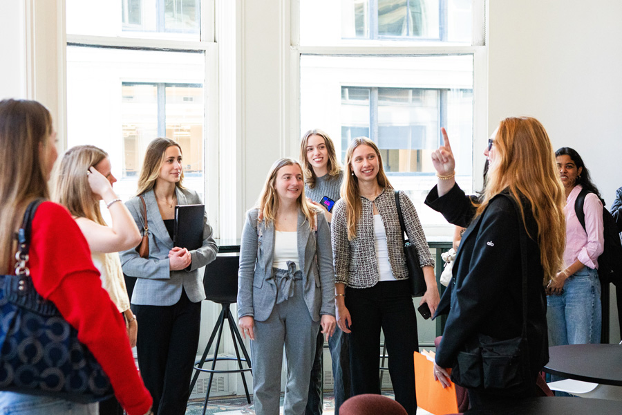 A group of students smile and interact in a naturally lit, modern office space.