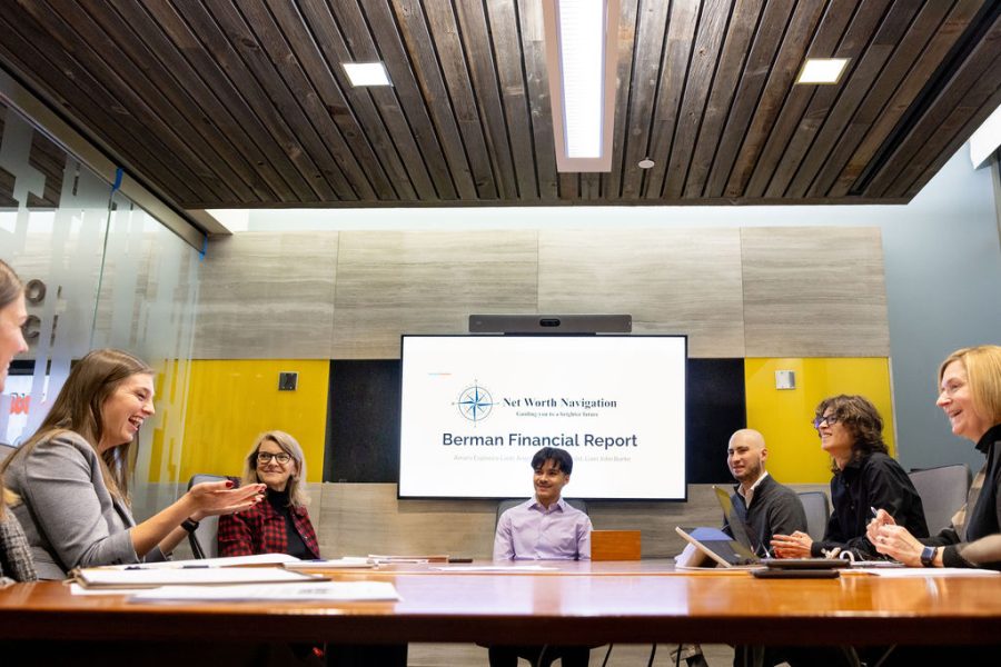 A group of alumni, faculty and students sit around a large table in a modern conference room. They are smiling and engaged in conversation.