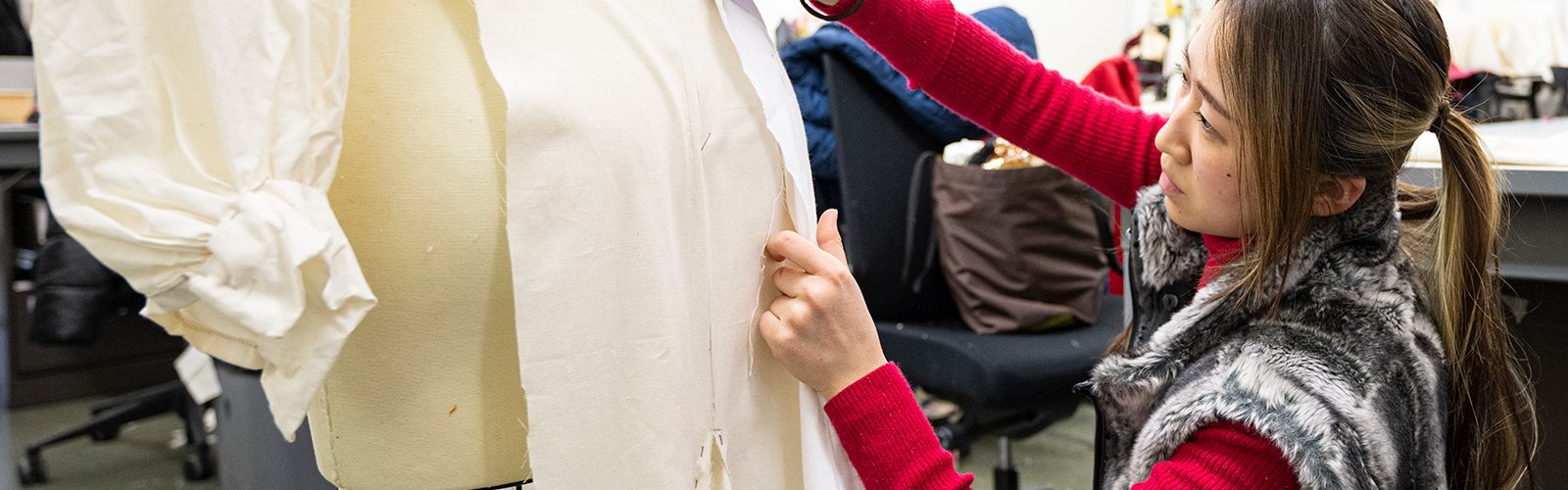 A student holds up white fabric against a body form as part of a garment they're making.