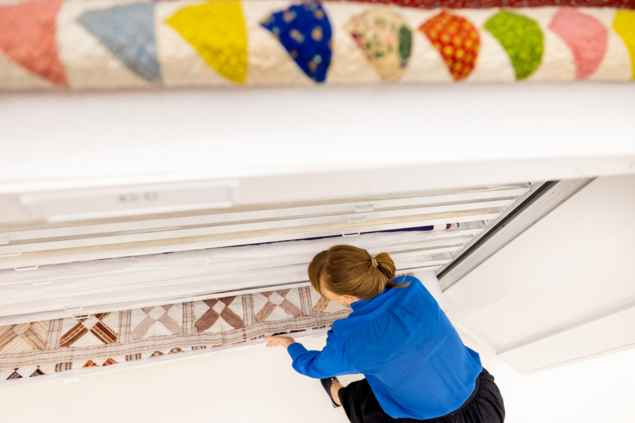 A woman with a blue shirt pulling a textile from white set of archival drawers.
