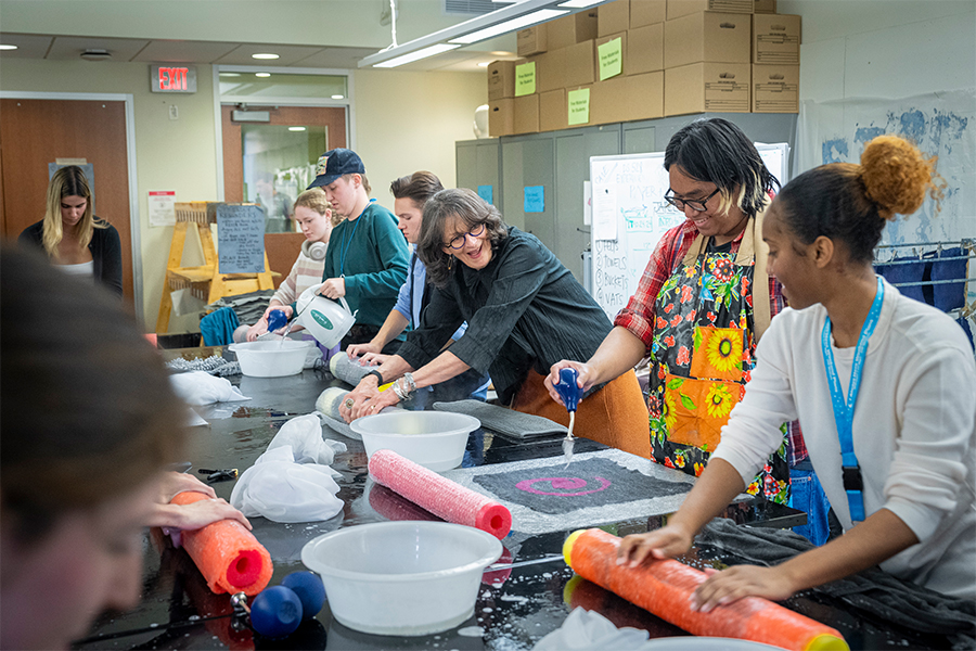 An instructor smiles with students while they're all making felt at a large table.