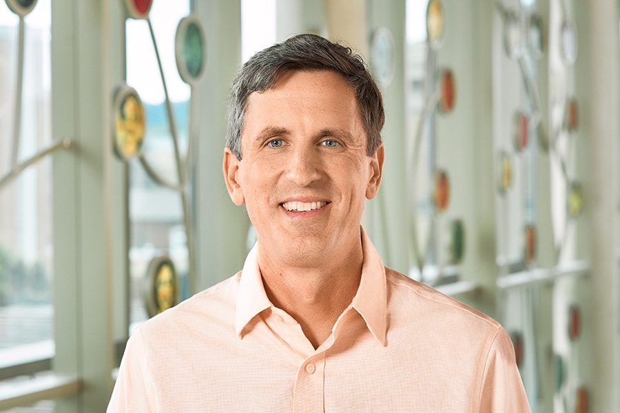 A white man smiling, with short brown hair, wearing a light orange shirt.