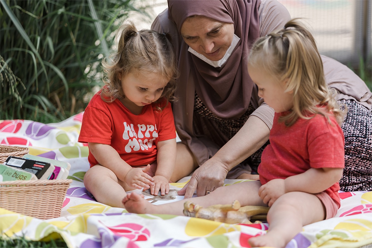 An adult points at a book and two children sit close to see.
