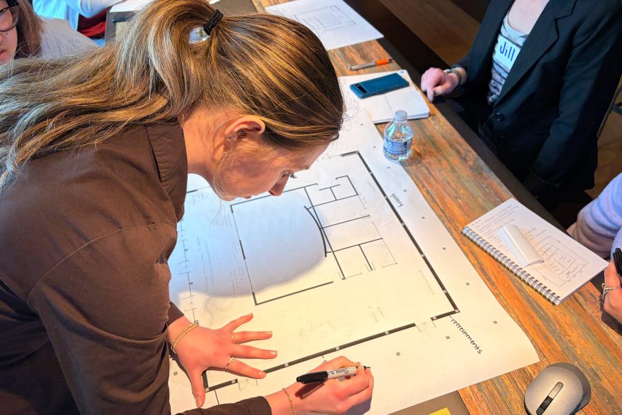 Student sketches details onto a large architectural floor plan.