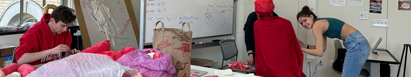 Students work in an art studio surrounded by red and pink fabric materials.