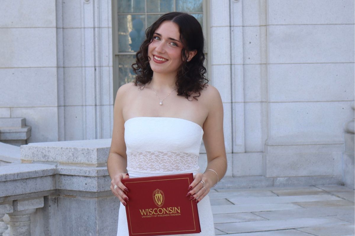 A young woman with dark, shoulder-length hair poses with a red UW–Madison diploma.