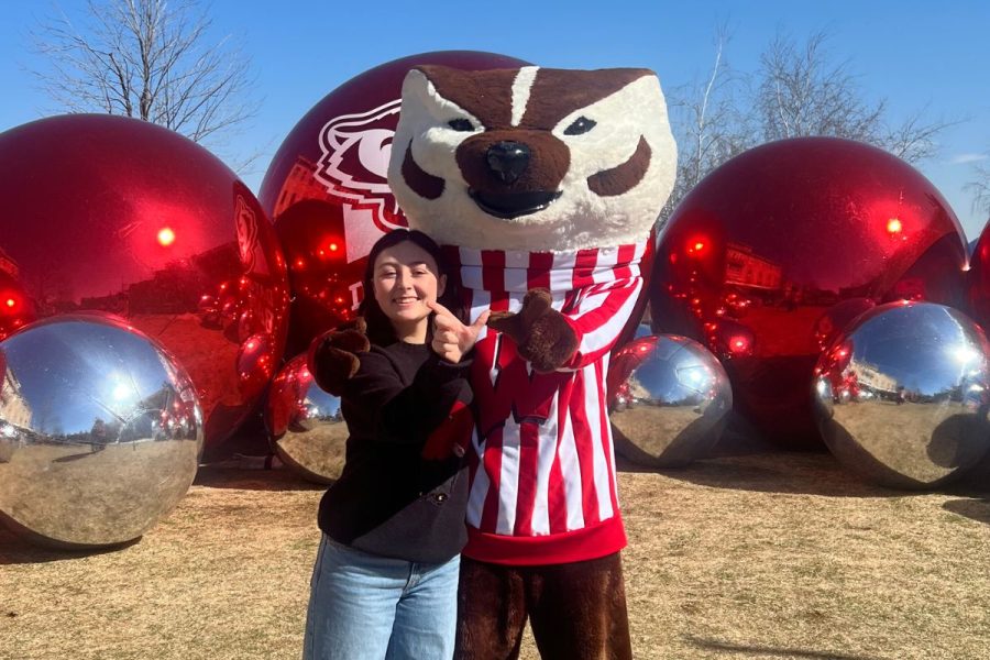 Sofia and UW–Madison mascot Bucky Badger stand in front of a giant metal silver and red orbs, holding up the "W" with their hands.
