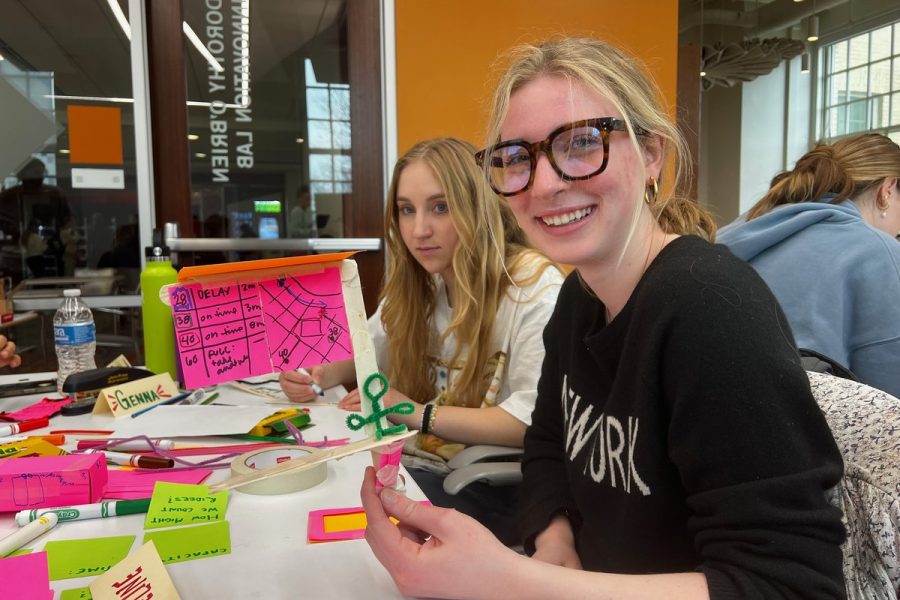 Smiling design student wearing glasses working on a colorful sticky-note brainstorming project alongside classmates in an innovation lab