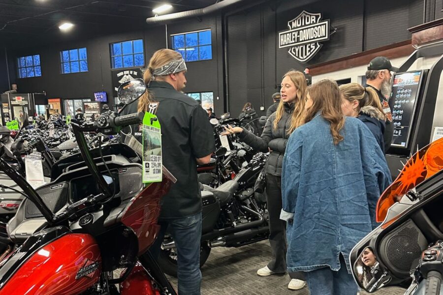 Group of students talking to a salesperson in a Harley-Davidson motorcycle showroom.