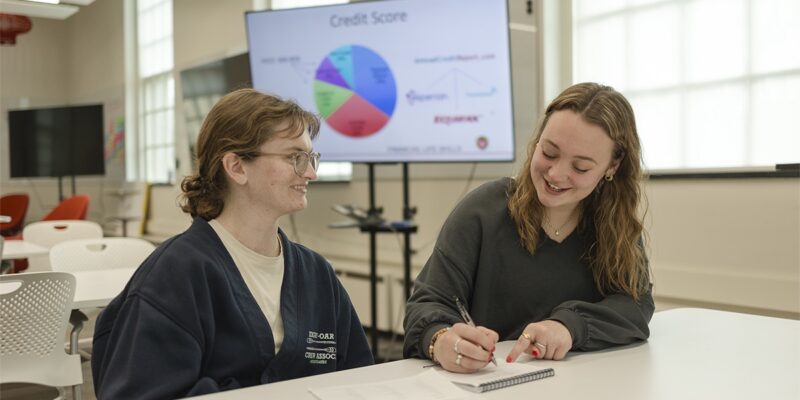 BadgerSense coach Alexis Swaney '26 meets with a student peer. A credit score pie chart is in the background.