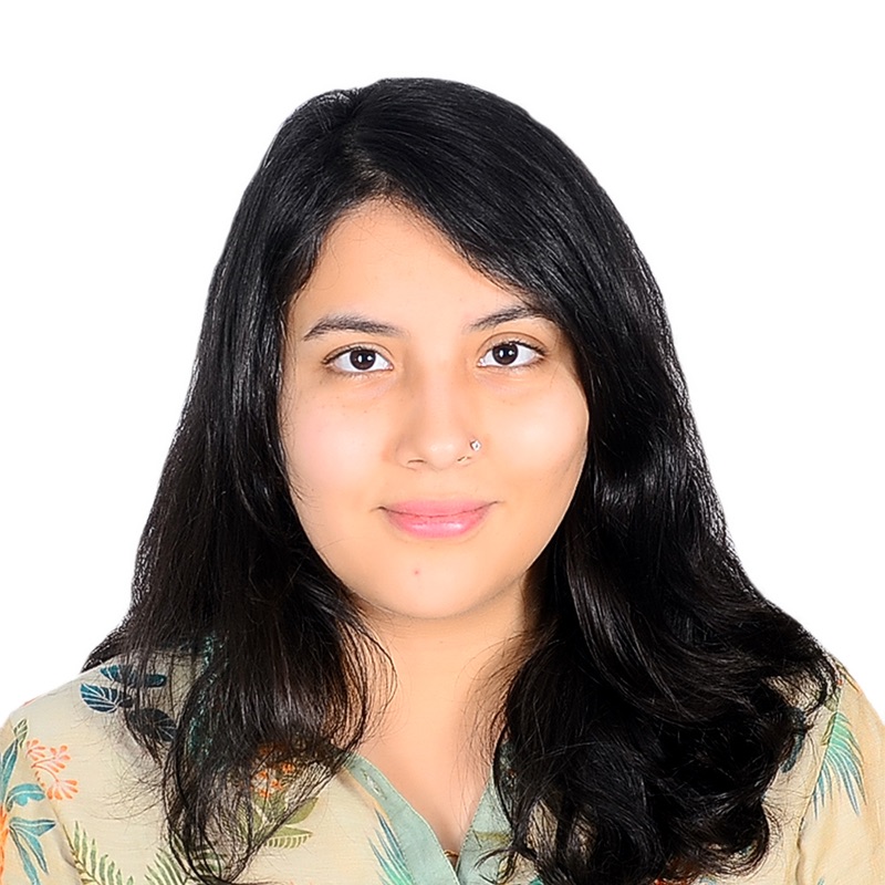 A brown woman smiling, with blackish-brown wavy hair, wearing colorful patterned shirt.