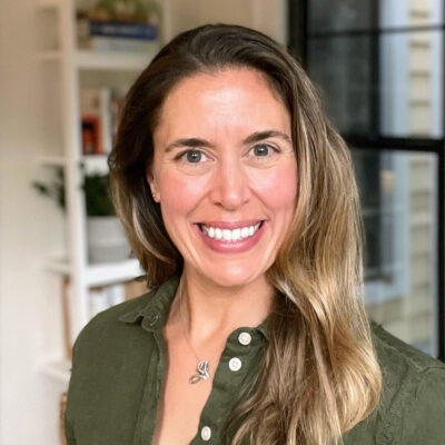 A white woman with light brown hair and green eyes smiling, wearing a dark green button-down shirt.