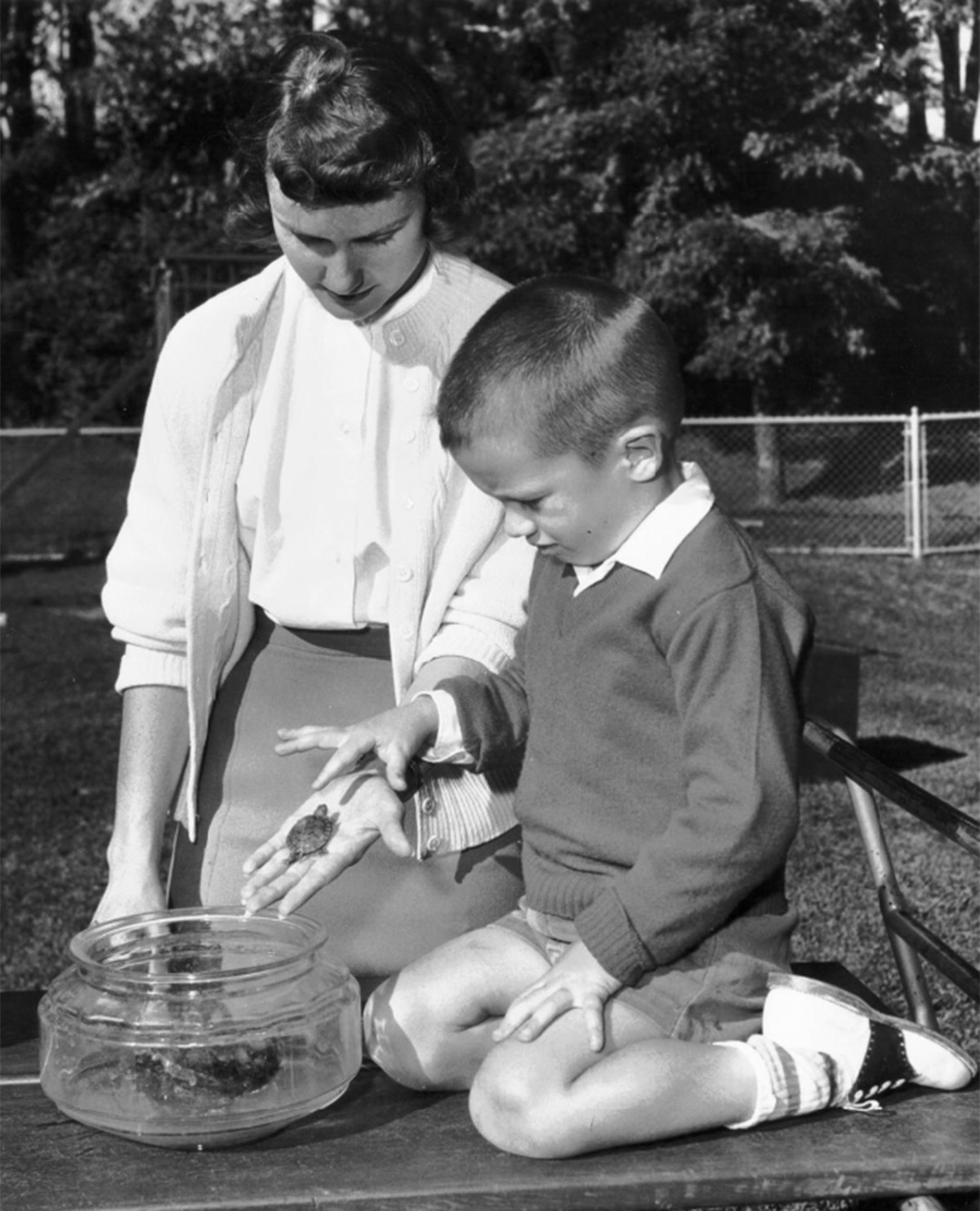 Black and white photo outdoors of an adult holding a small turtle in their hand for a child to explore.