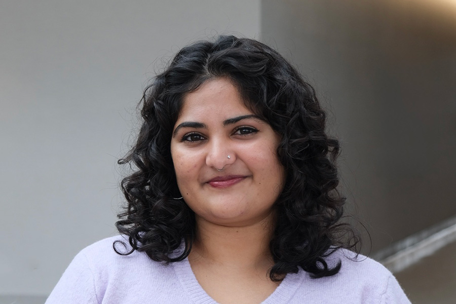 Portrait of a smiling woman with dark curly hair wearing a lavender sweater.